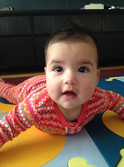 A baby, lying on a rug, props herself up, so her dad can take a photo and send it to her grandparents using Do Camera.